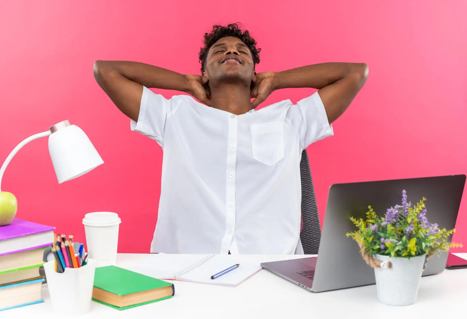 pleased young afro american student sitting with closed eyes desk with-school tools putting hands his head isolated pink wall